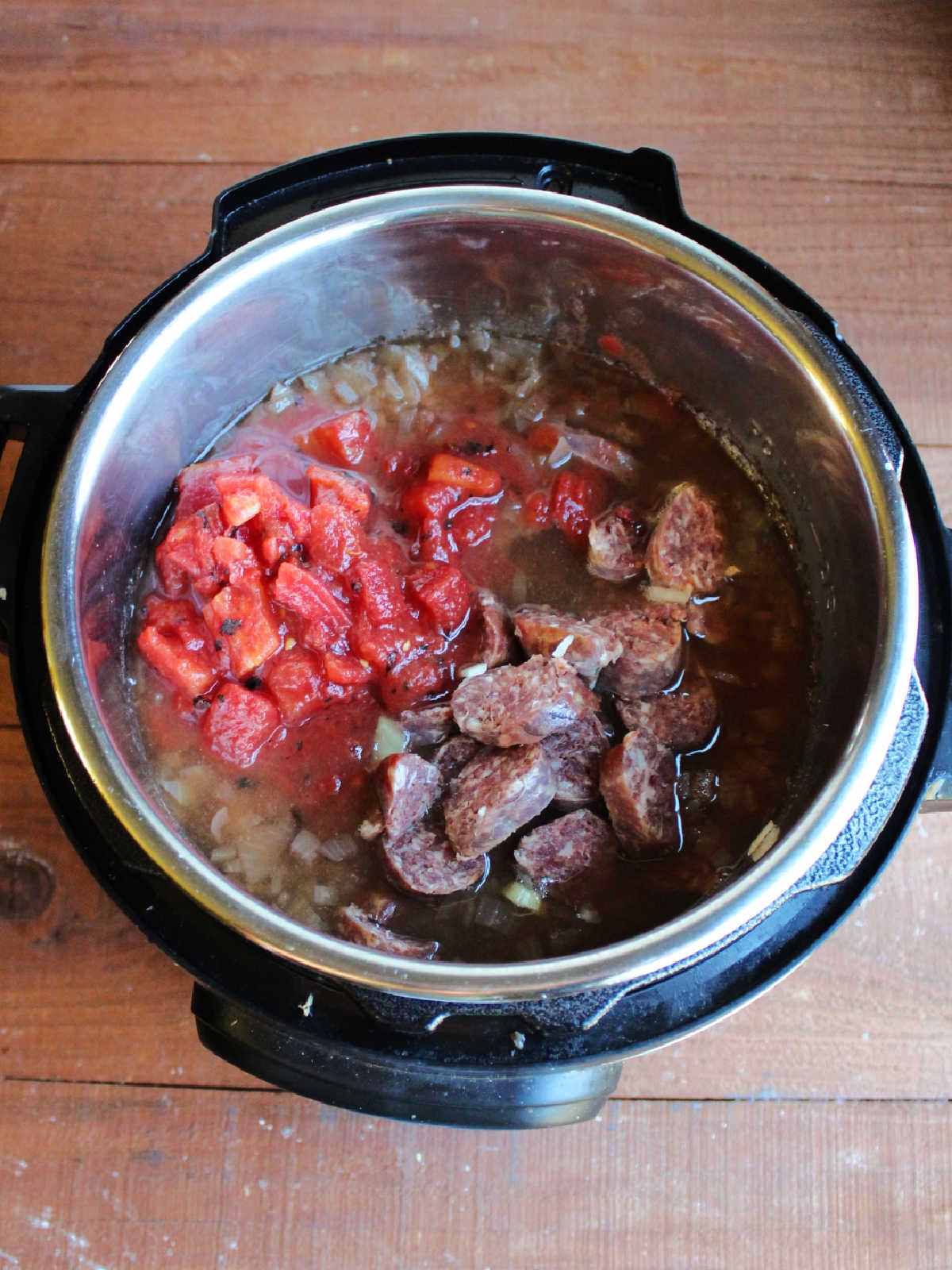 Diced tomatoes and sliced kielbasa in Instant Pot with bean soup, ready to finish cooking.