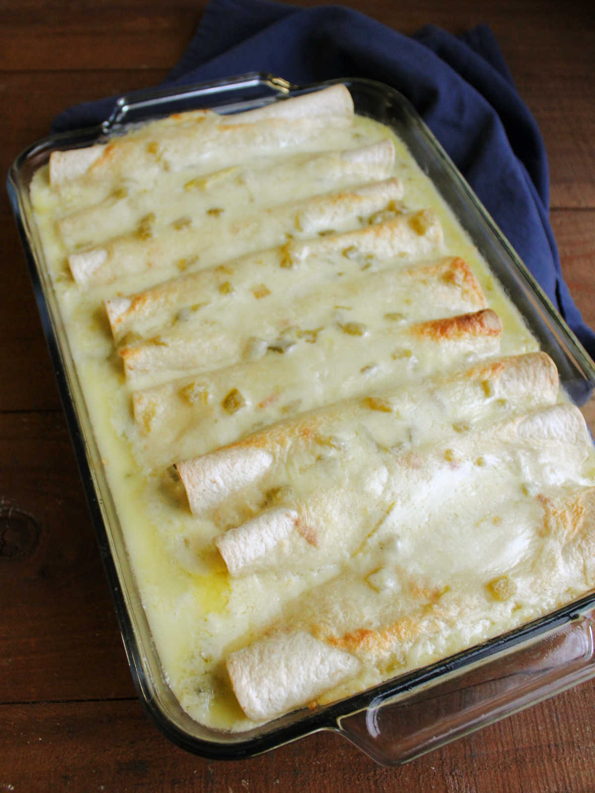 Glass baking dish filled with freshly baked breakfast enchiladas baked in creamy cheese sauce with spots of light golden brown toastiness.