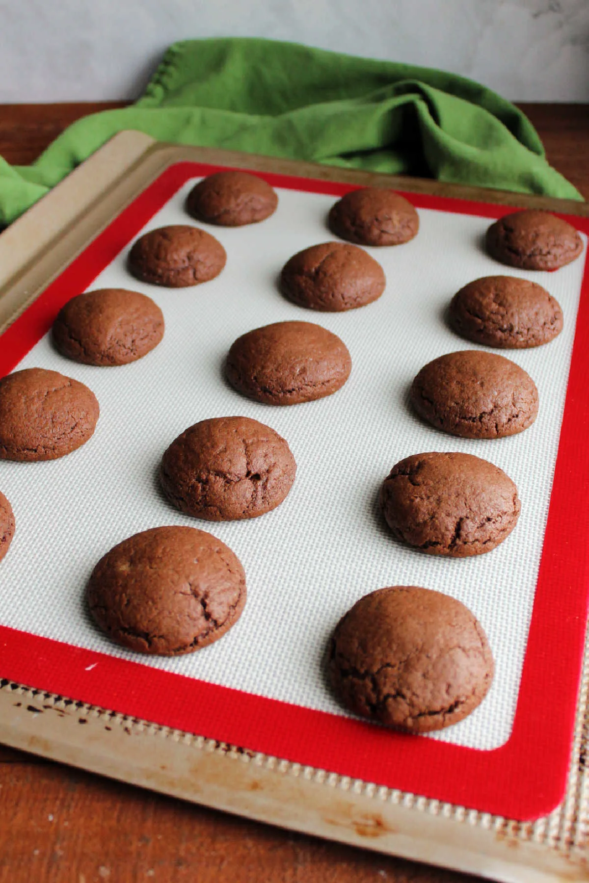 Puffy freshly baked chocolate cookies on silicone mat lined cookie tray.