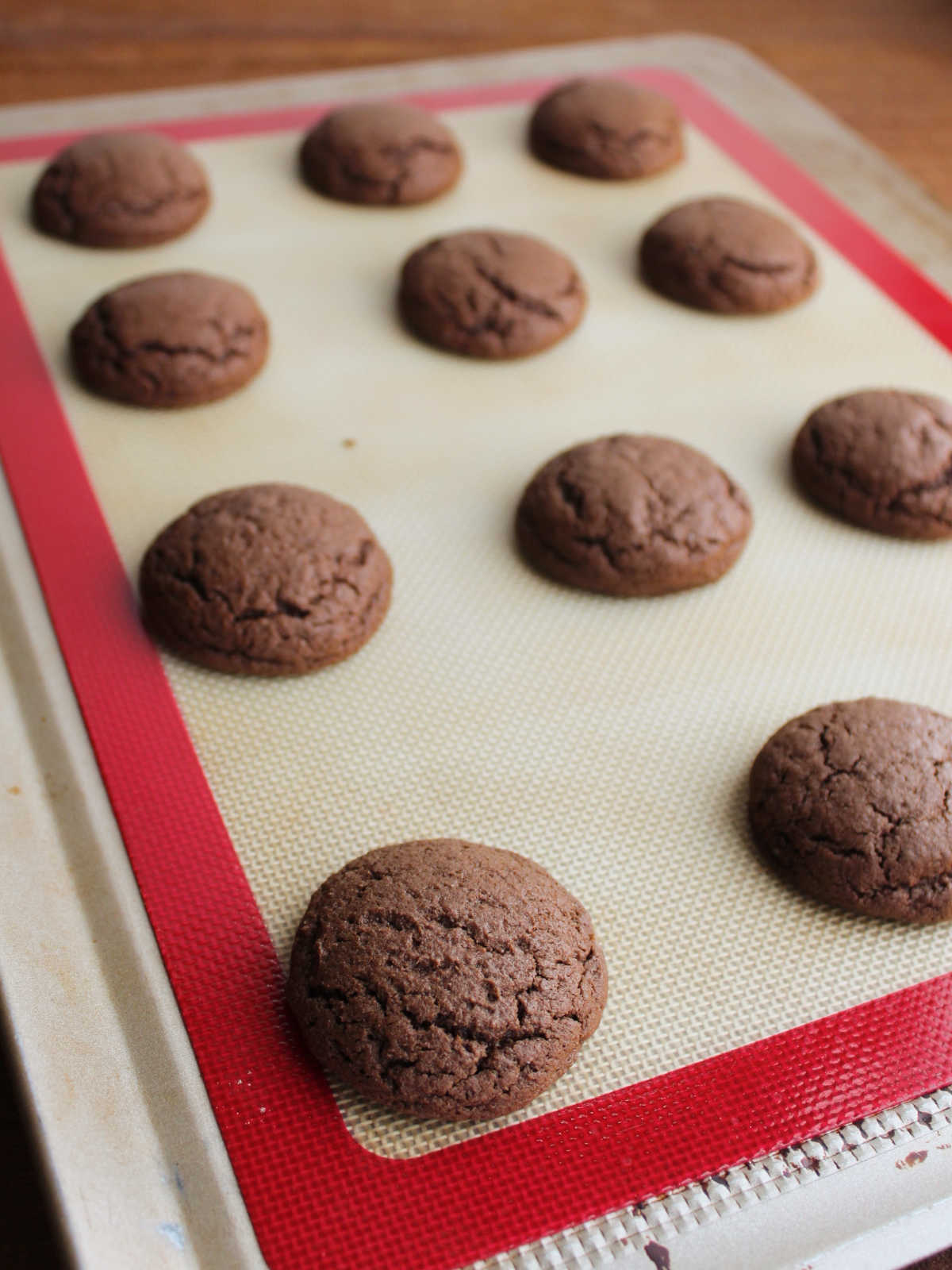 Freshly baked chocolate cookies on pan, showing fluffy texture and round shape.