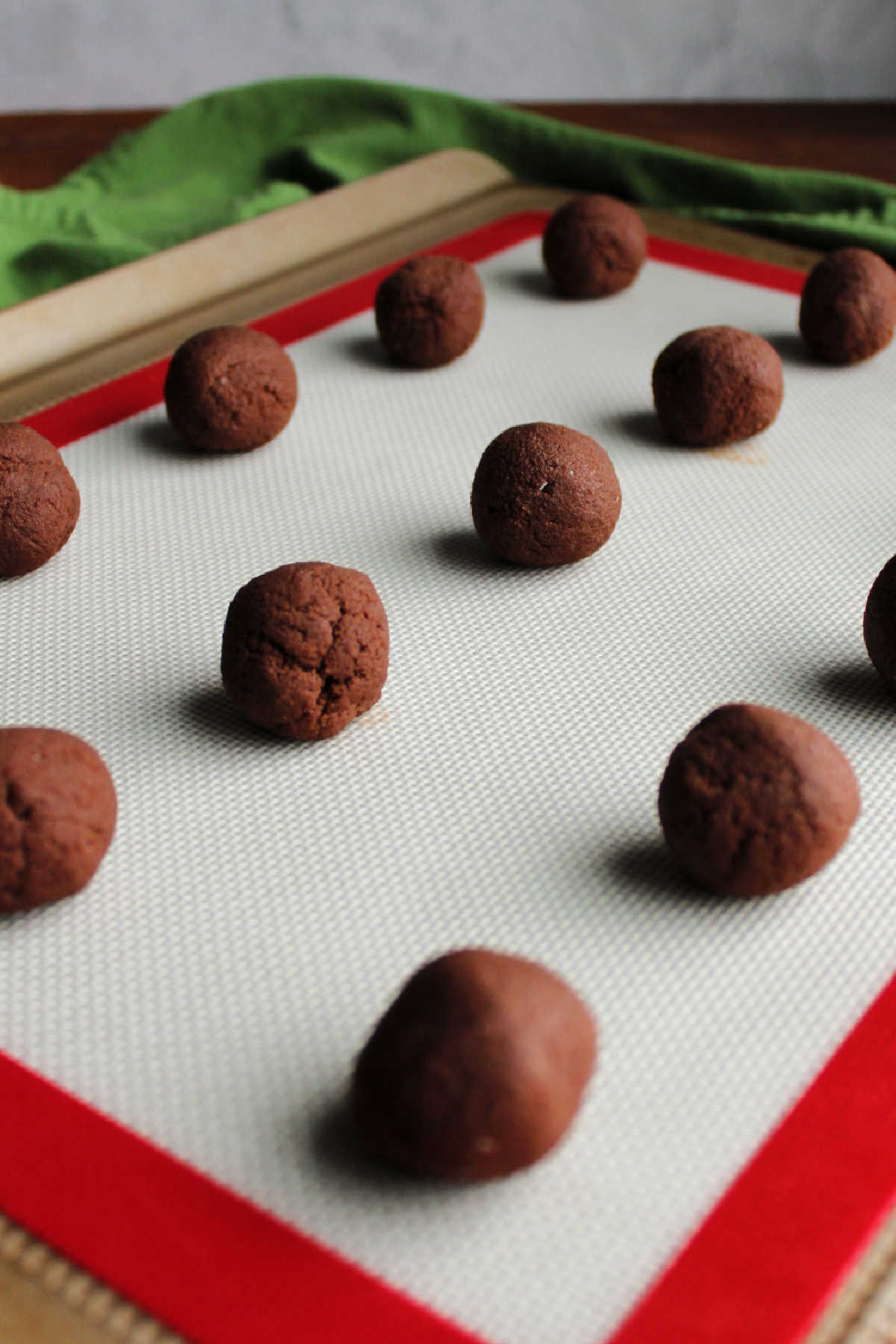 Balls of chocolate cookie dough on silicone mat lined cookie tray.