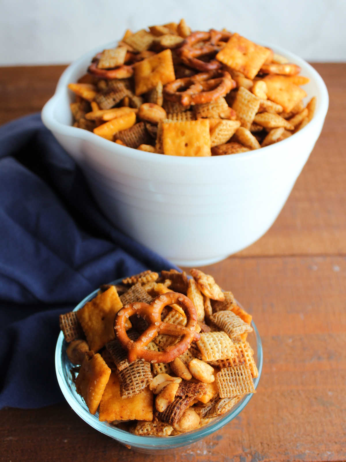 Larger white serving bowl filled with seasoned and smoked bbq Chex mix next to a smaller bowl of chex mix, ready to eat. 