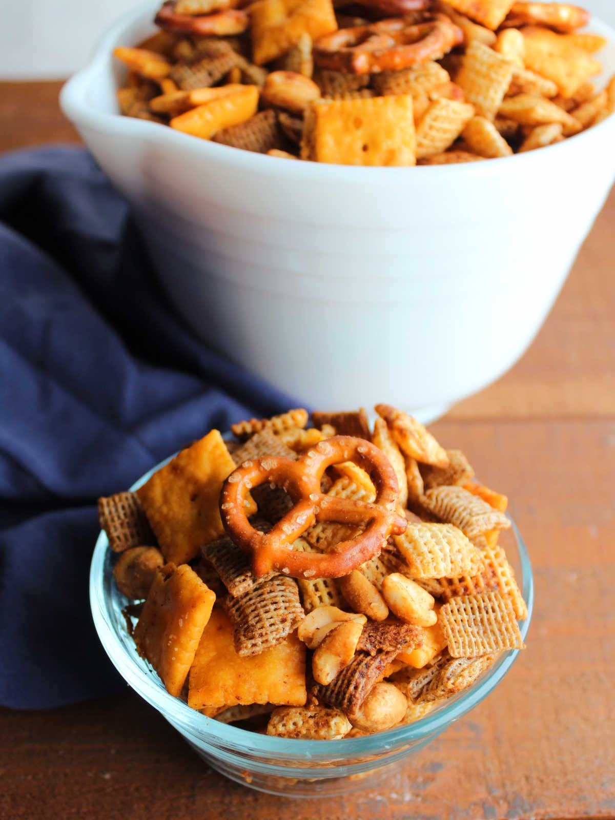 Small glass bowl of smoked chex mix with larger bowl of smoked bbq chex mix in the background.