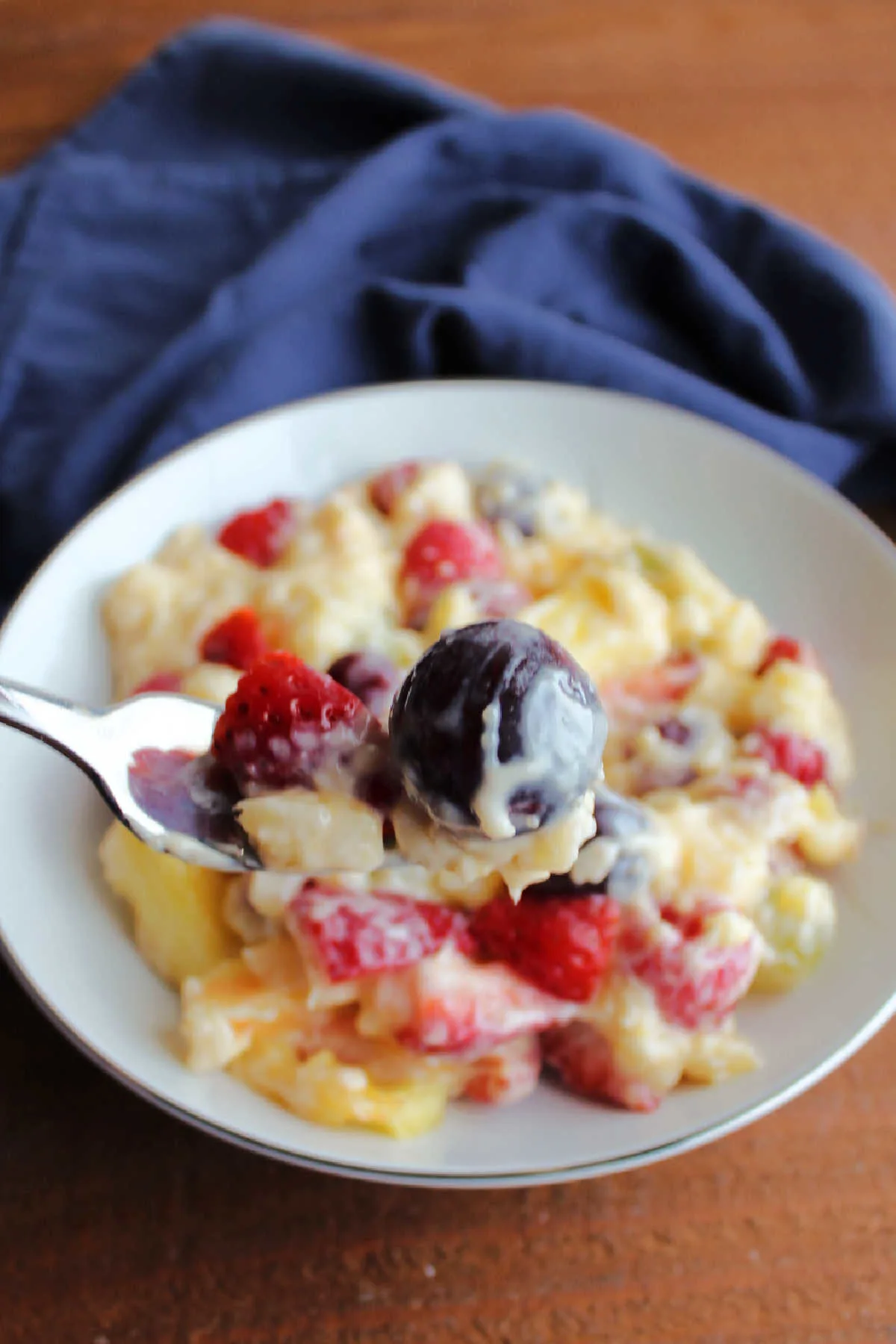 Fork with red grape, strawberry slices, and pineapple coated in creamy vanilla pudding mixture.