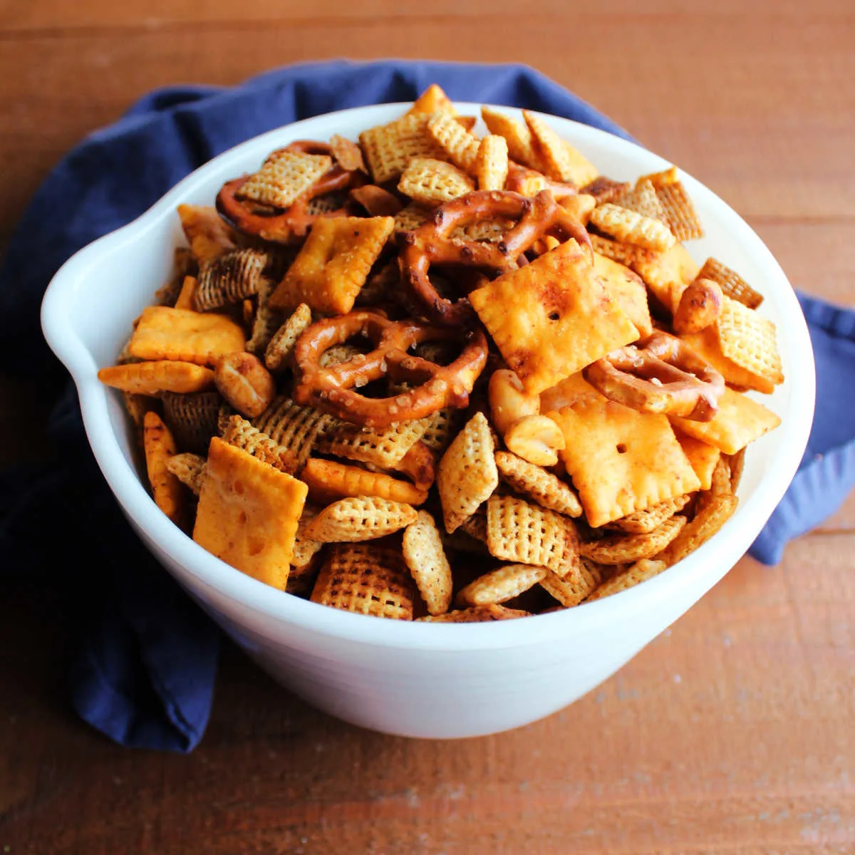 Antique white bowl filled with smokey bbq chex mix made from cheese crackers, cereal, peanuts, and pretzels.