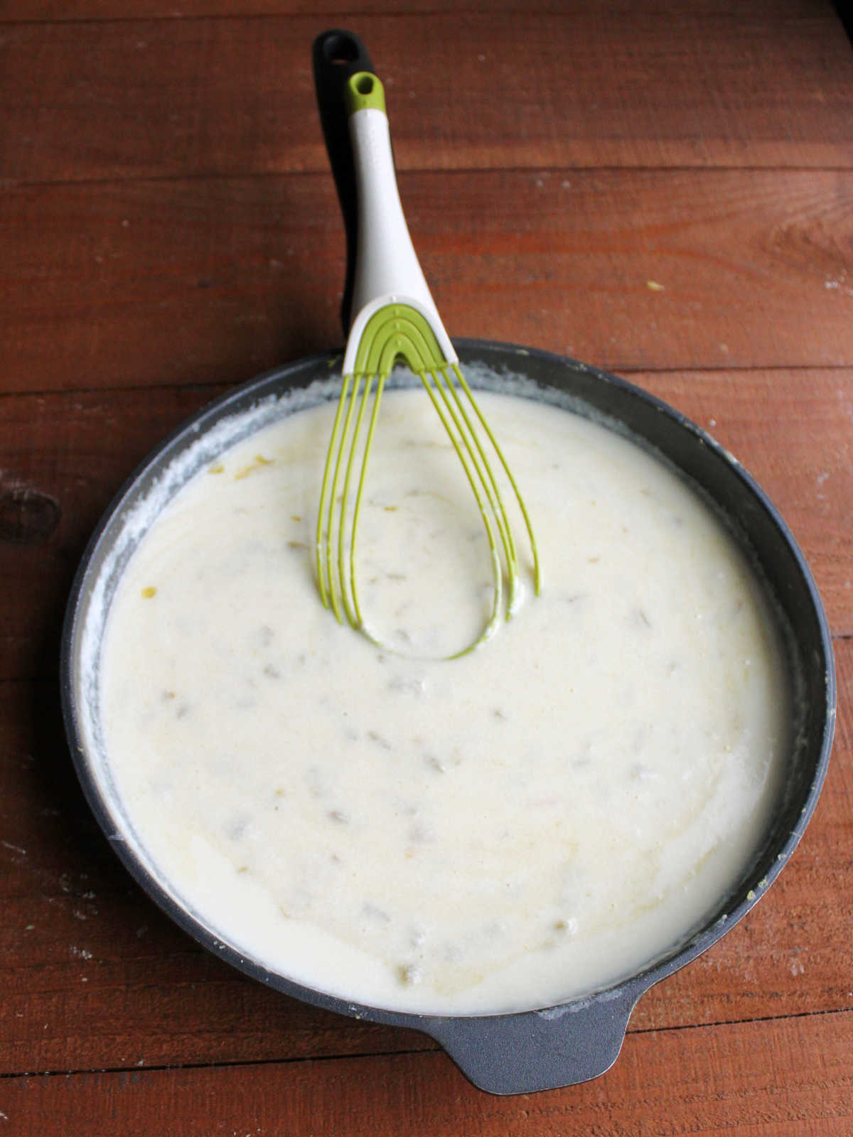 Skillet with smooth white cheese sauce with bits of green chilies inside.