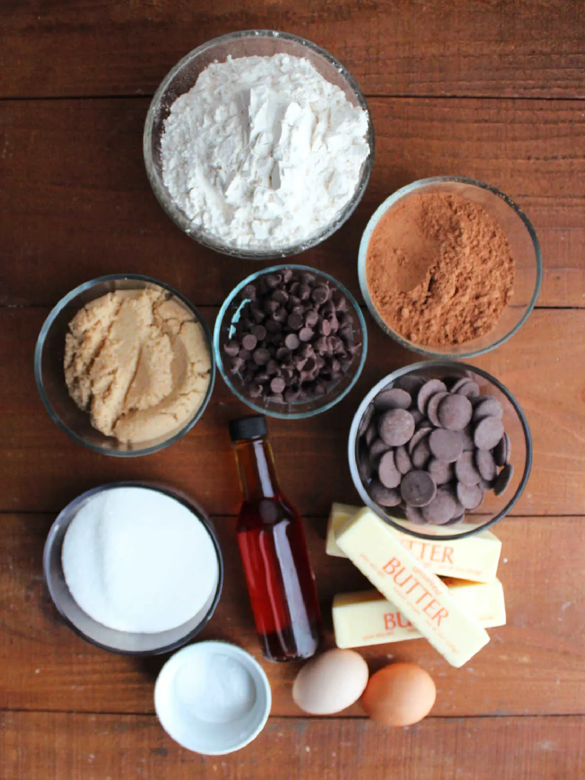 Ingredients including butter, sugar, brown sugar, eggs, vanilla, flour, cocoa powder, salt, baking soda, chocolate chips, and chocolate melting wafers ready to be made into chocolate paw print cookies.