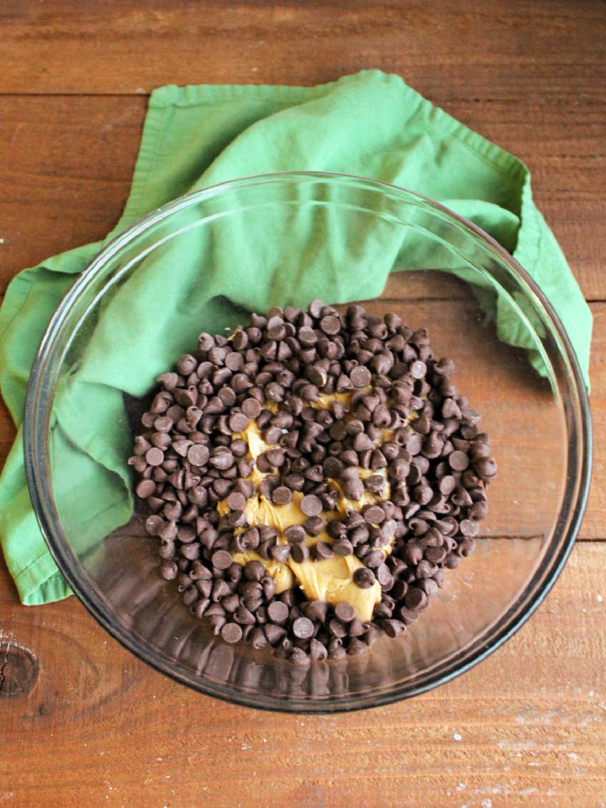 Large glass mixing bowl with creamy peanut butter and chocolate chips inside.