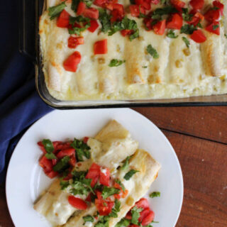 Pan of breakfast enchiladas next to a plate with two enchiladas topped with extra tomato and cilantro, ready to eat.