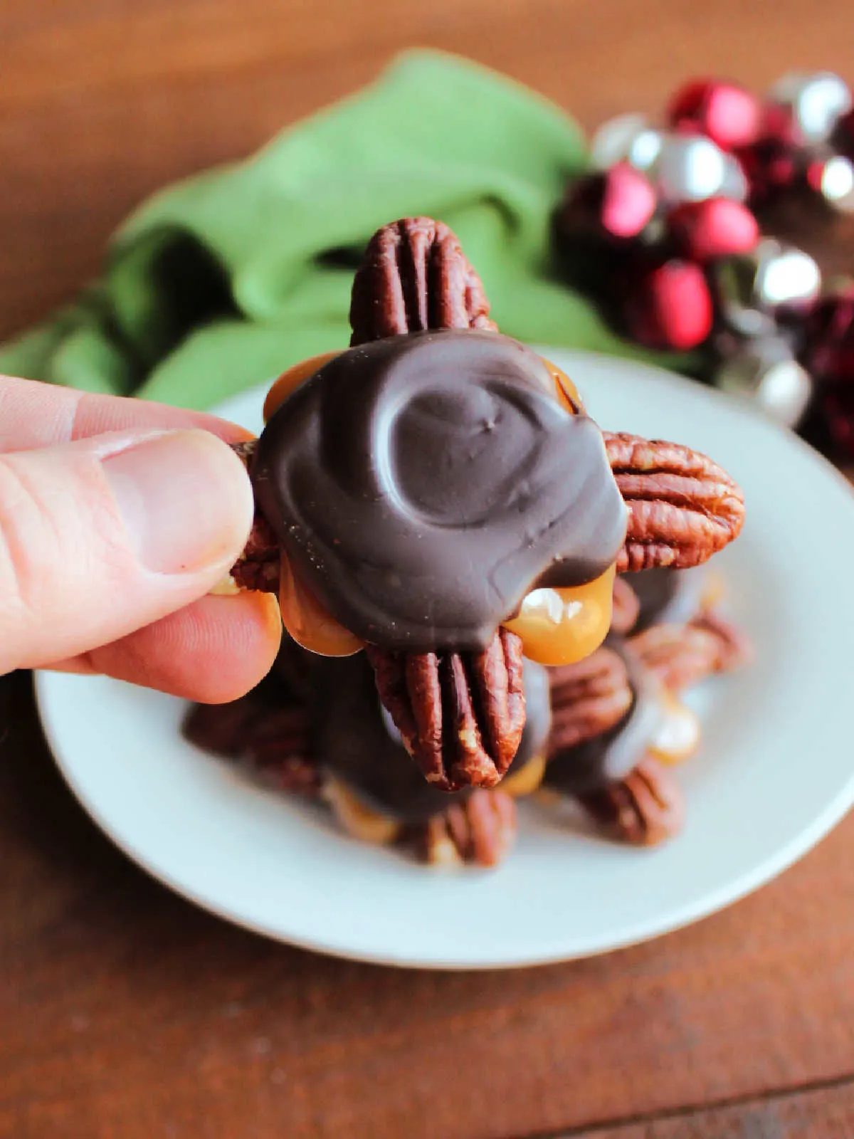 Hand holding homemade turtle candy with pecans, rich caramel, and chocolate.