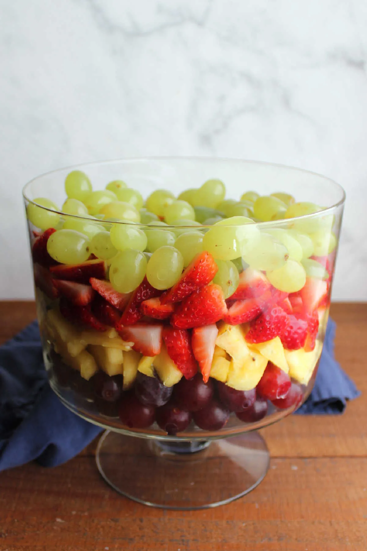 Glass trifle bowl filled with layers of red grapes, fresh pineapple chunks, sliced strawberries, and green grapes.