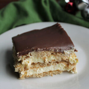 Slice of eclair cake with vanilla pudding mixture, graham crackers, and fudge icing.
