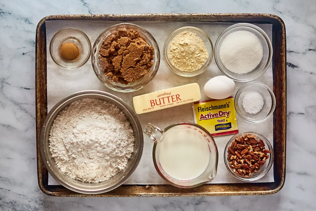 Ingredients including flour, butter, yeast, sugar, brown sugar, cinnamon, corn meal, egg, milk, and salt ready to be made into sticky buns.