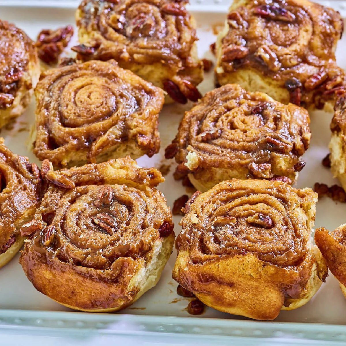 Tray of caramel pecan rolls showing the cinnamon filling spiral, soft dough, gooey caramel, and chopped pecans, ready to eat.