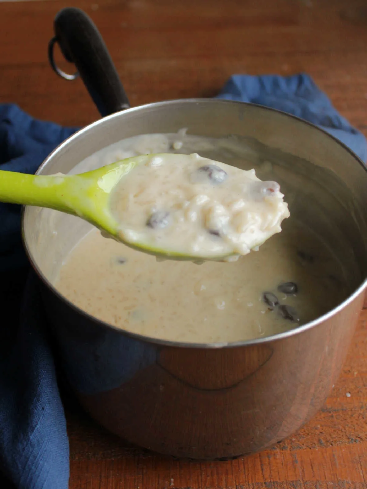Serving spoon of cooked condensed milk rice pudding mixture showing how it is still loose when it is hot.