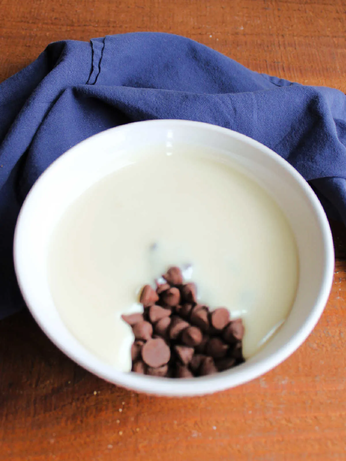Sweetened condensed milk and chocolate chips in a bowl, ready to be melted into chocolate icing for the eclair cake.