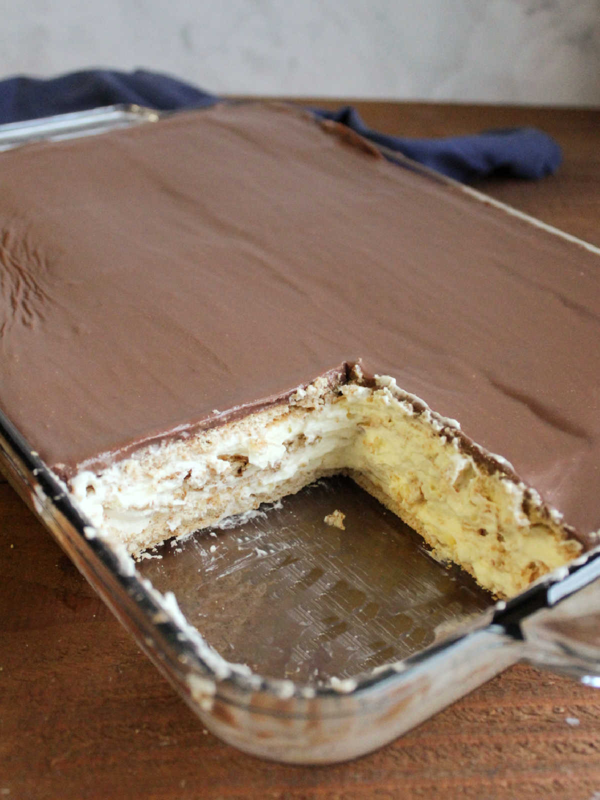 Pan of eclair cake with a piece missing showing layers of graham crackers and pudding topped my smooth fudgy chocolate icing. 