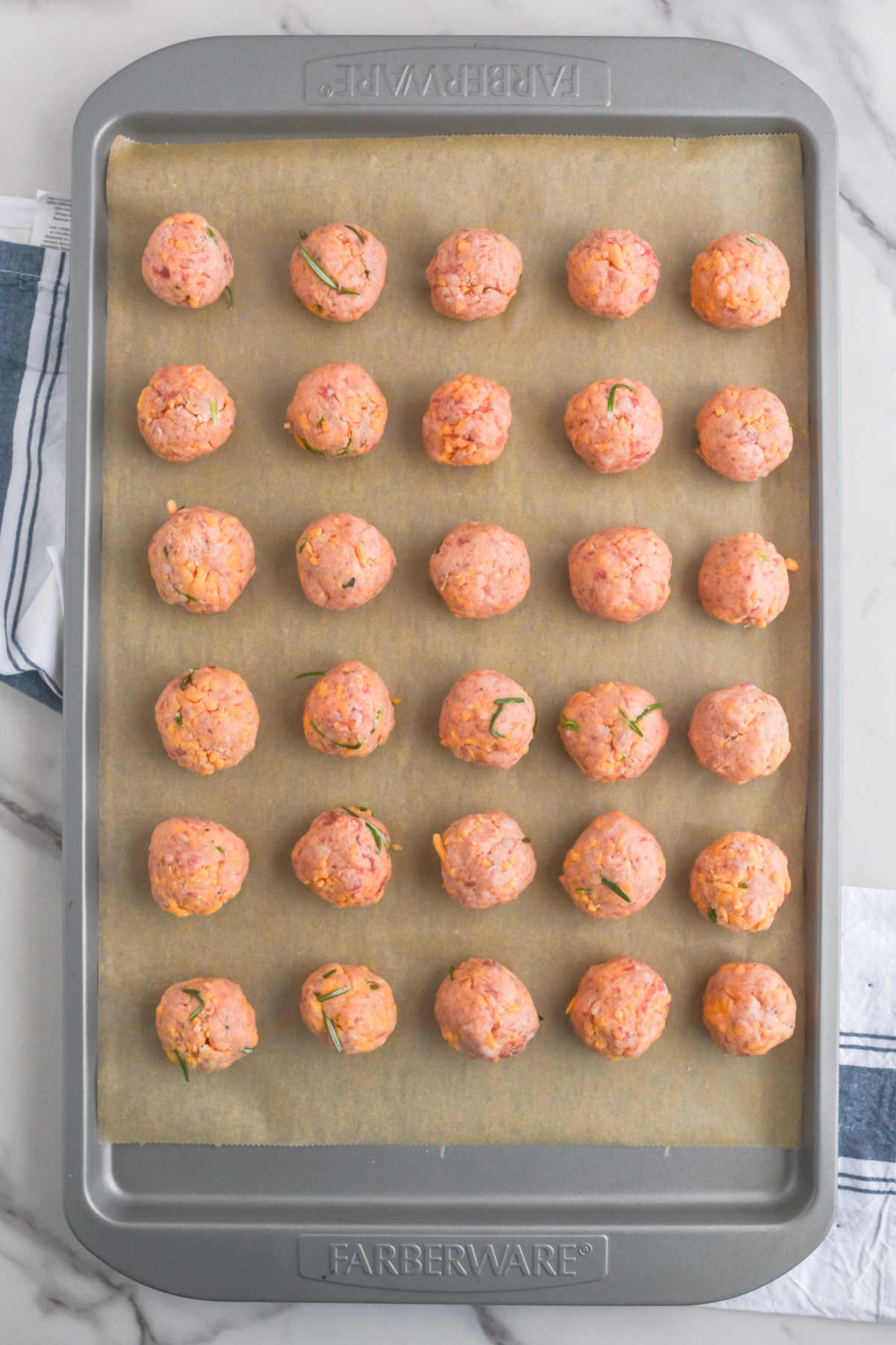 Baking sheet of round balls of sausage mixture arranged over parchment paper, ready to go in the oven. 