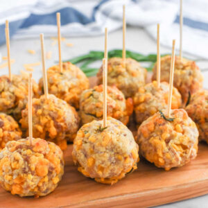 Sausage balls arranged on a wooden platter with toothpicks for easy serving showing the small balls with lots of cheddar cheese and some rosemary inside.