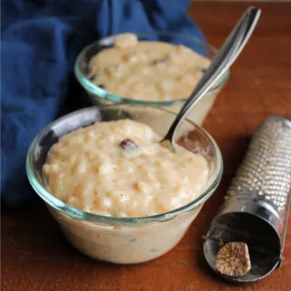 Two small glass bowls of creamy condensed milk rice pudding with raisins next to a nutmeg grater.