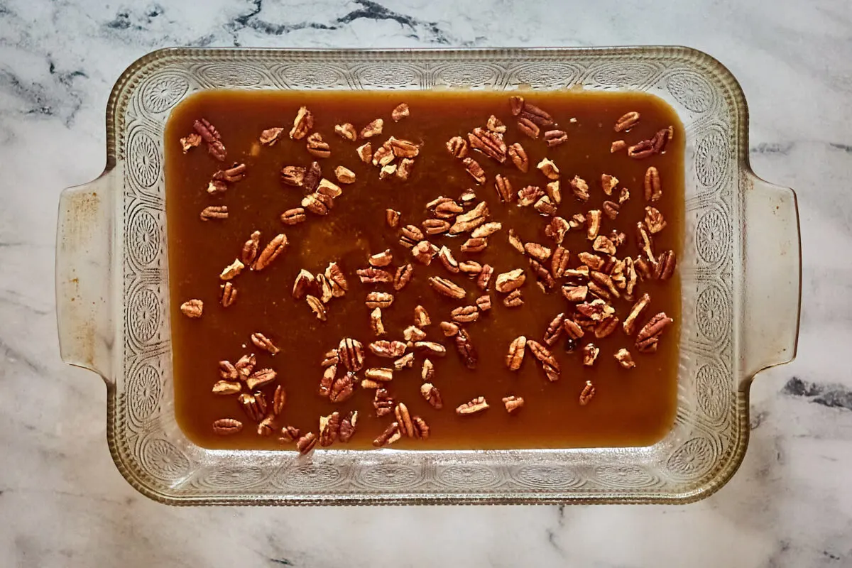 9x13-inch pan with warm caramel mixture and chopped pecans inside.