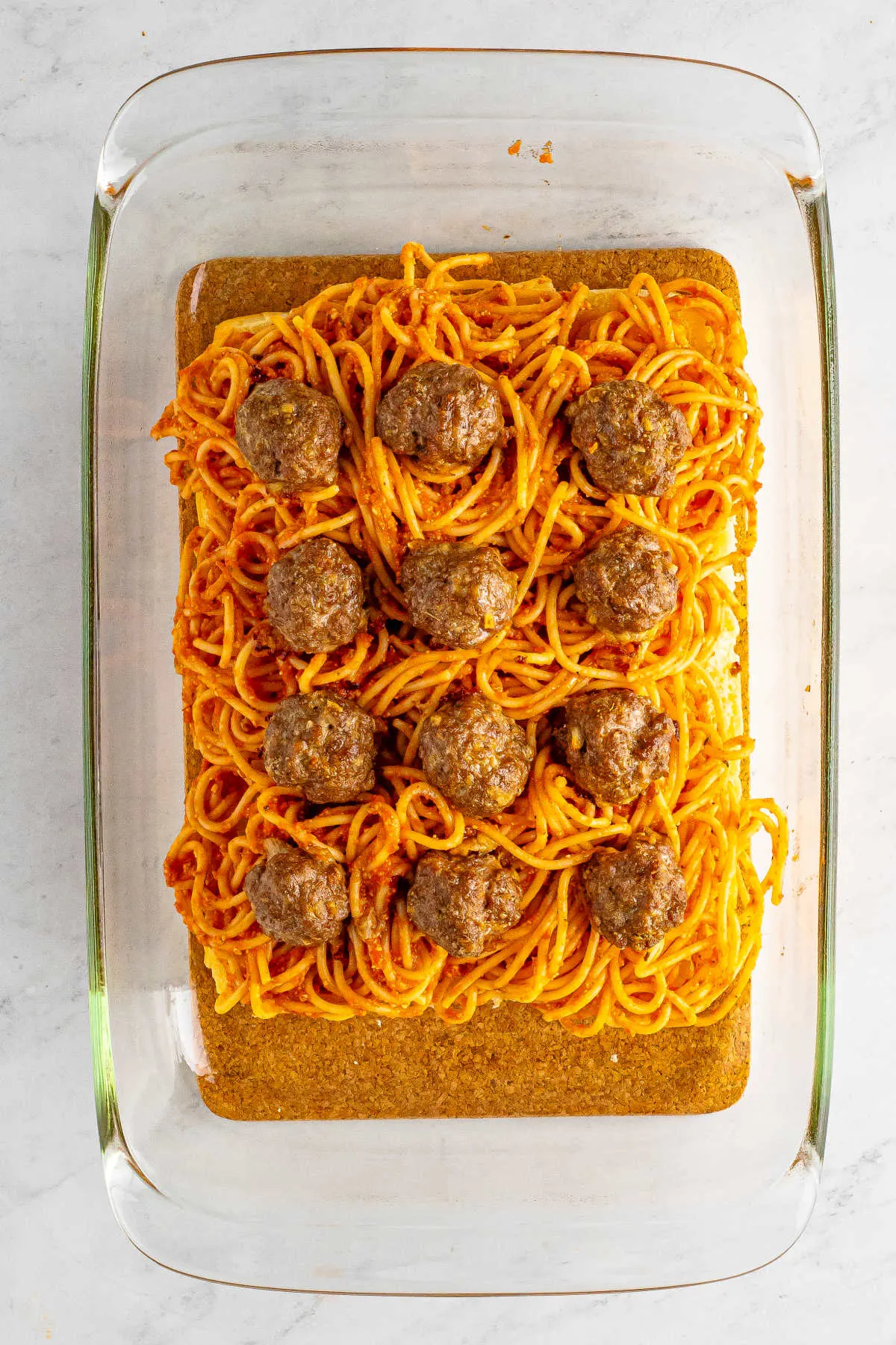 Spaghetti tossed with marinara sauce and cooked meatballs arranged over the bottom half of the sweet rolls in a 9x13-inch pan.