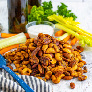 Pile of buffalo ranch roasted nuts in front of celery sticks, carrot sticks, and a bowl of ranch dip, ready for a party.