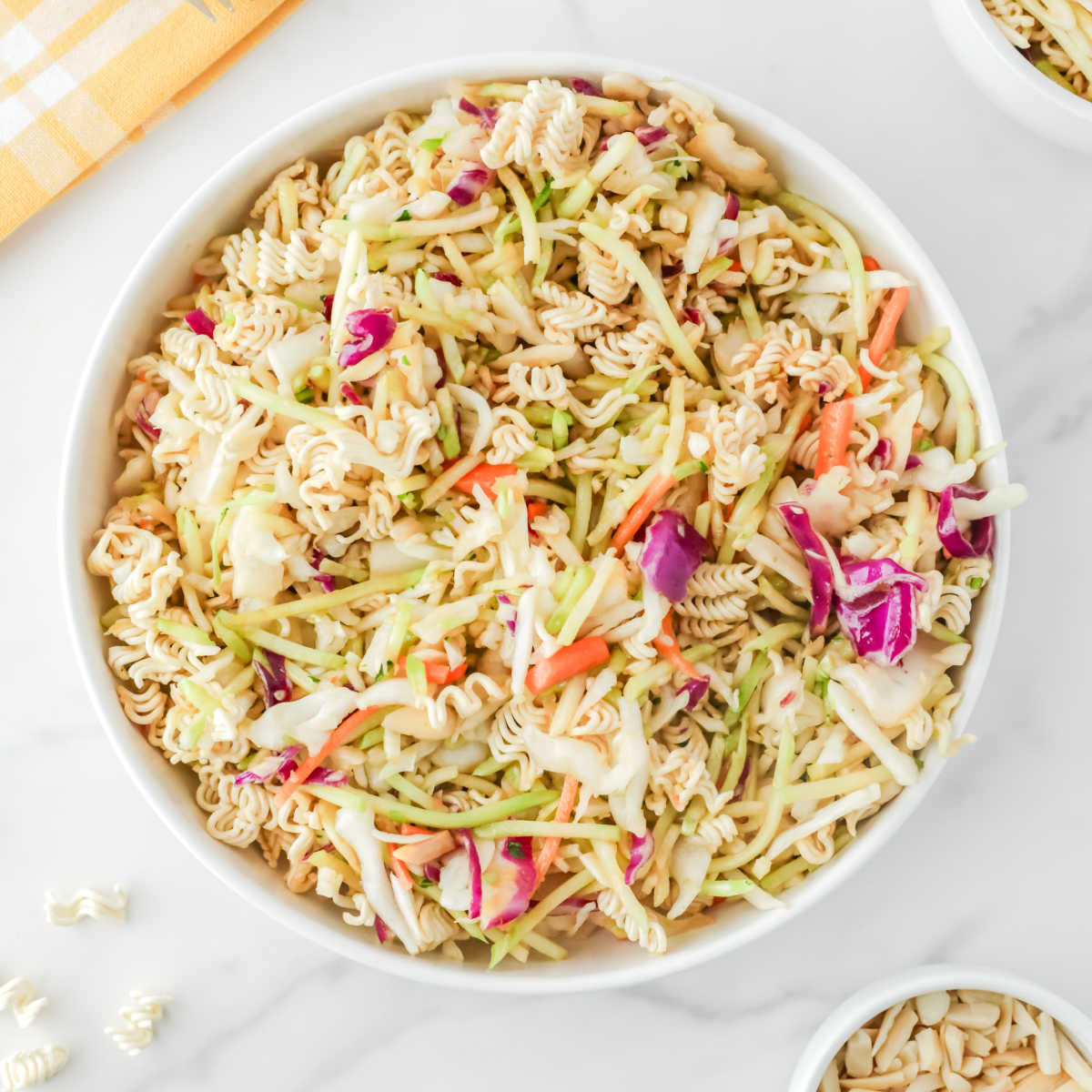Serving bowl of ramen noodle coleslaw with cabbage, broccoli, carrots, almonds, and bits of crunchy ramen noodles all in a light soy sauce vinaigrette.
