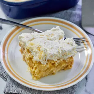 Piece of pineapple poke cake with condensed milk and fluffy white pineapple frosting on small plate with fork, ready to eat.