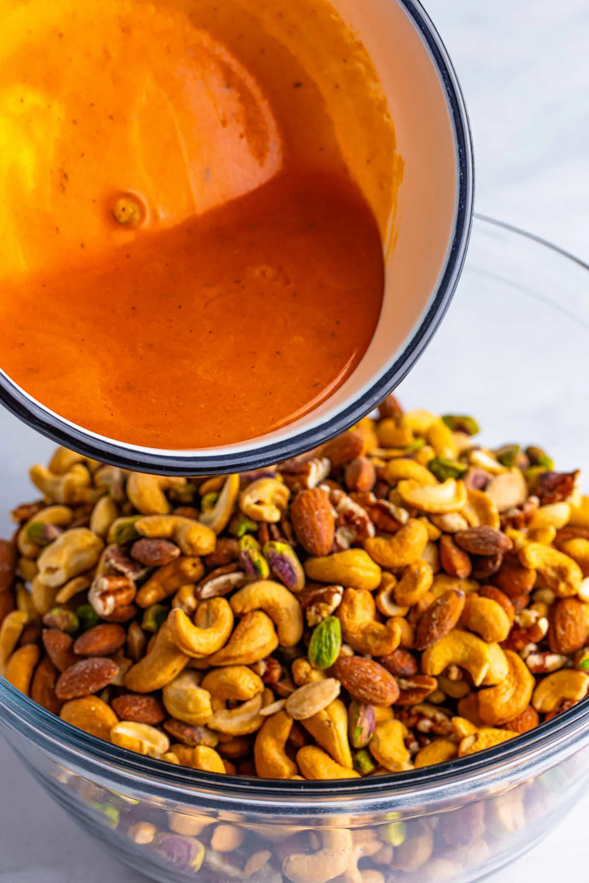 Pouring buttery buffalo ranch sauce over a bowl of mixed nuts.