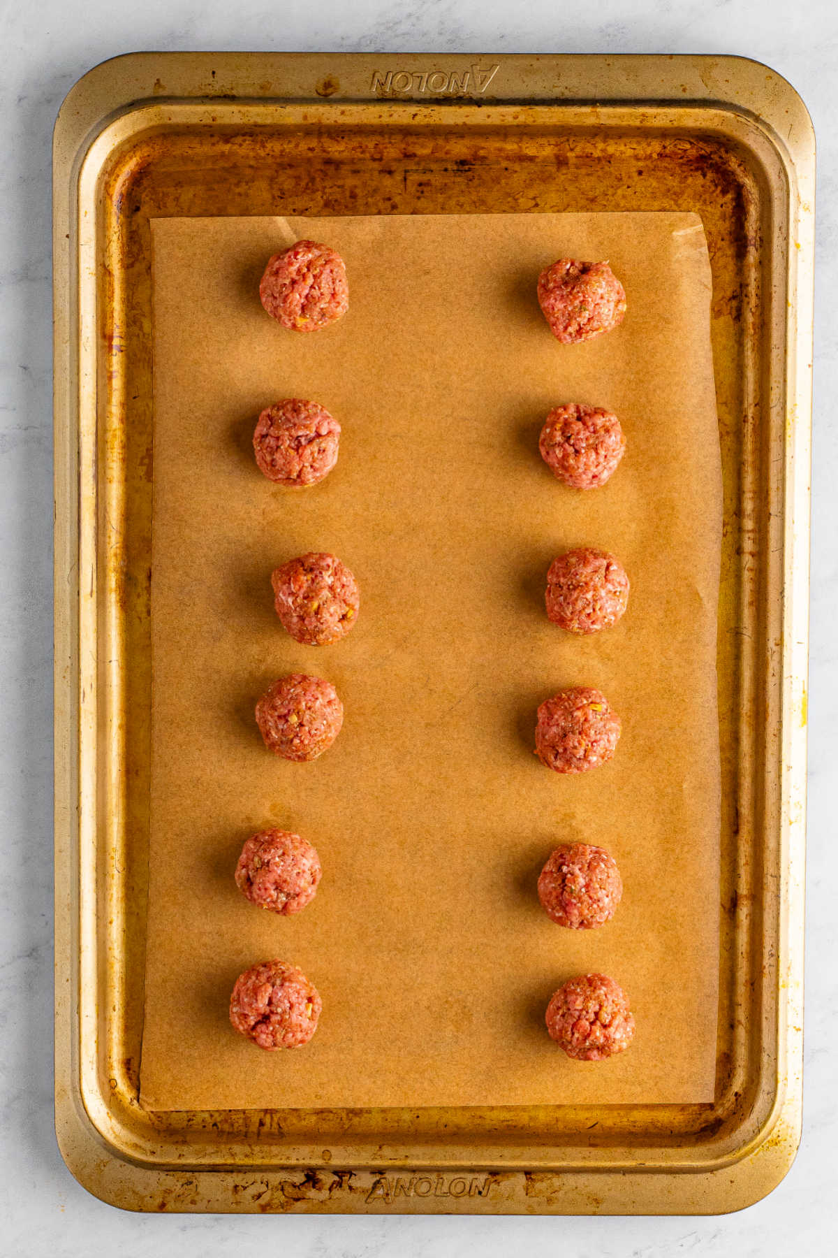 Raw meatballs on a parchment paper lined pan, ready to be baked.