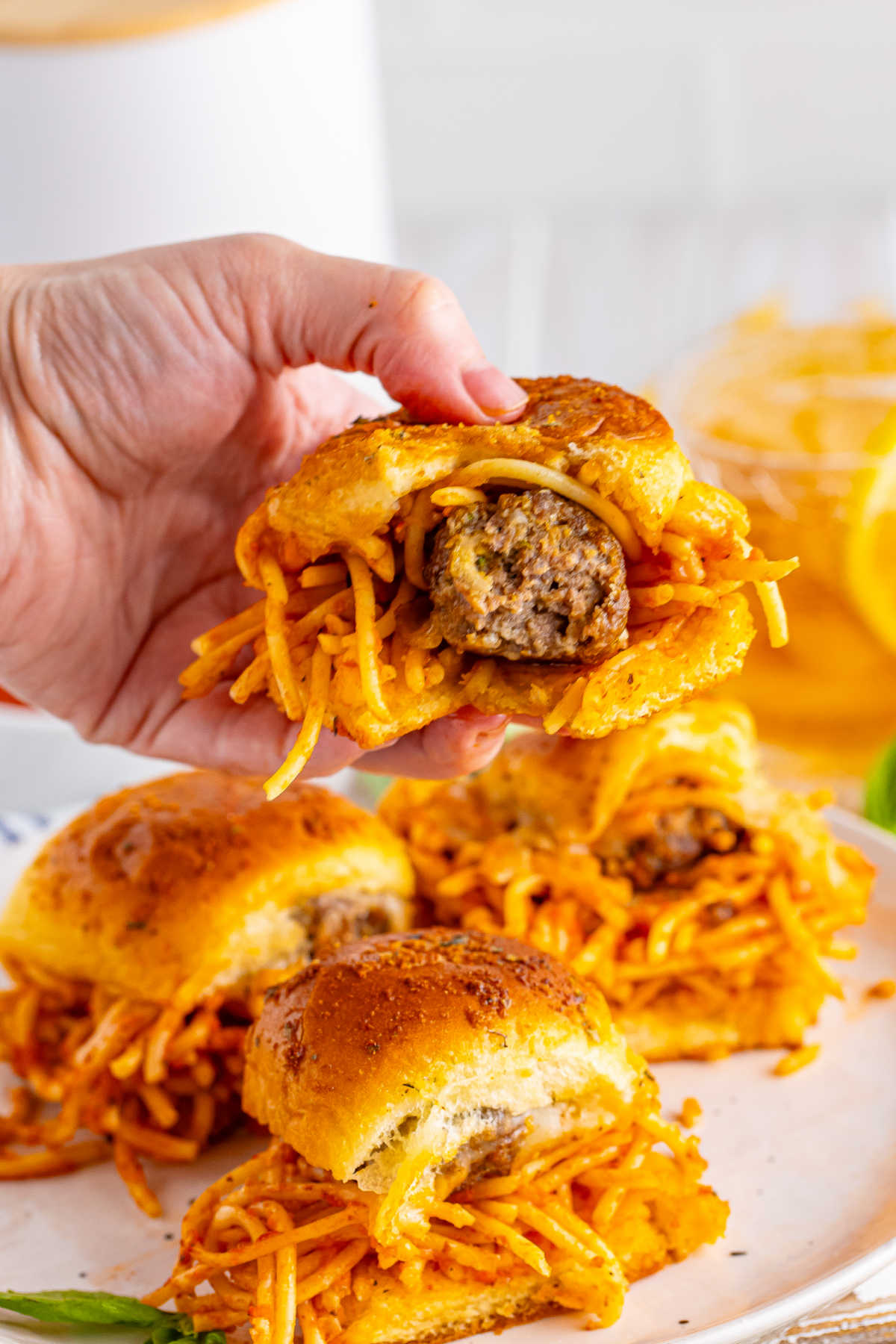 Hand holding a spaghetti and meatball slider with a bite missing showing the inside of the homemade meatball inside. 