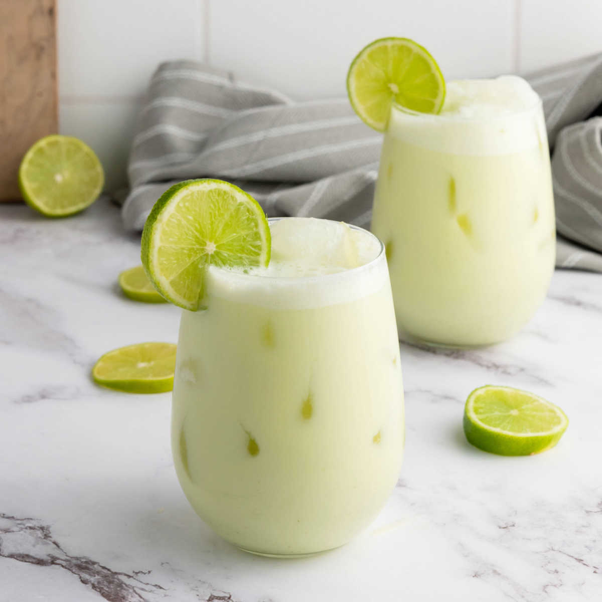 Two glasses filled with creamy limeade, plenty of ice and garnished with a slice of lime, ready to drink.