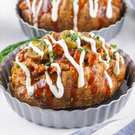 Pulled Pork Stuffed Baked Potatoes 1 Close up of a baked potato loaded with melted cheese, pulled pork, bbq sauce, sour cream, jalapenos, and chives.