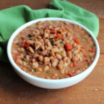 Serving bowl filled with cooked pinto beans in broth made with beer, onions, and jalapenos with bits of diced tomatoes and cilantro mixed in ready to be served as frijoles borrachos.