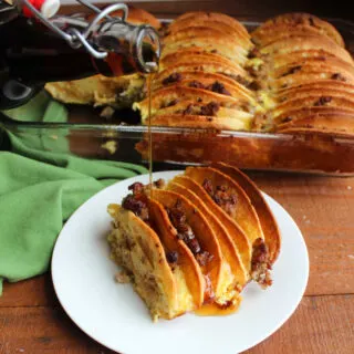 Pouring maple syrup over a slice of breakfast casserole with pancakes with crumbled sausage between the layers baked in an egg mixture.