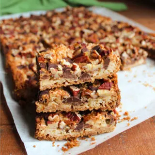 Magic cookie bars with graham cracker crumb crust topped with coconut, pecans, and chocolate chips stacked on top of each other, ready to eat.