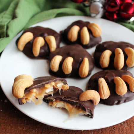Homemade Bear Paw Candies 2 Close up of a plate of bear paw candies with one cut broken open showing caramel and cashew center with chocolate coating and cashew bear claws.