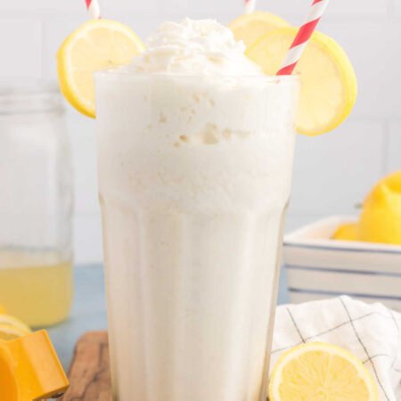 Easy Frosted Lemonade Recipe 2 Close glass of frosted lemonade with creamy milkshake texture topped with whipped cream and a slice of fresh lemon, ready to drink.