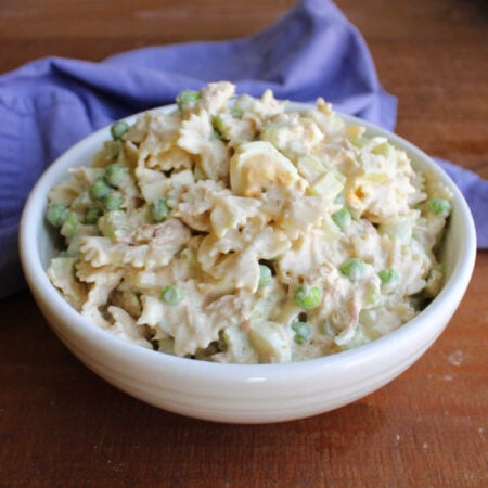 Tuna Pasta Salad 1 Serving bowl pile high with creamy tuna pasta salad with peas, celery, and chunks of hard boiled eggs inside.