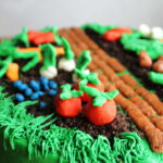 Close up of veggies made from white modeling chocolate dyed different colors and shaped then placed on top of a cake.