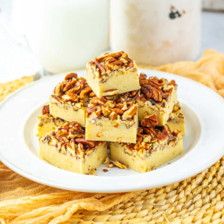 Pecan Pie Fudge 1 Stack of squares of pecan pie fudge with creamy base and toasted pecans on top on plate, ready to eat.