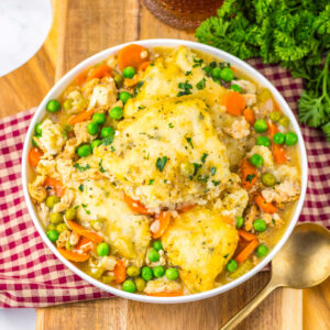 Crockpot Chicken and Dumplings 11 Bowl with chunks of chicken and veggies in creamy broth with big fluffy biscuits on top.