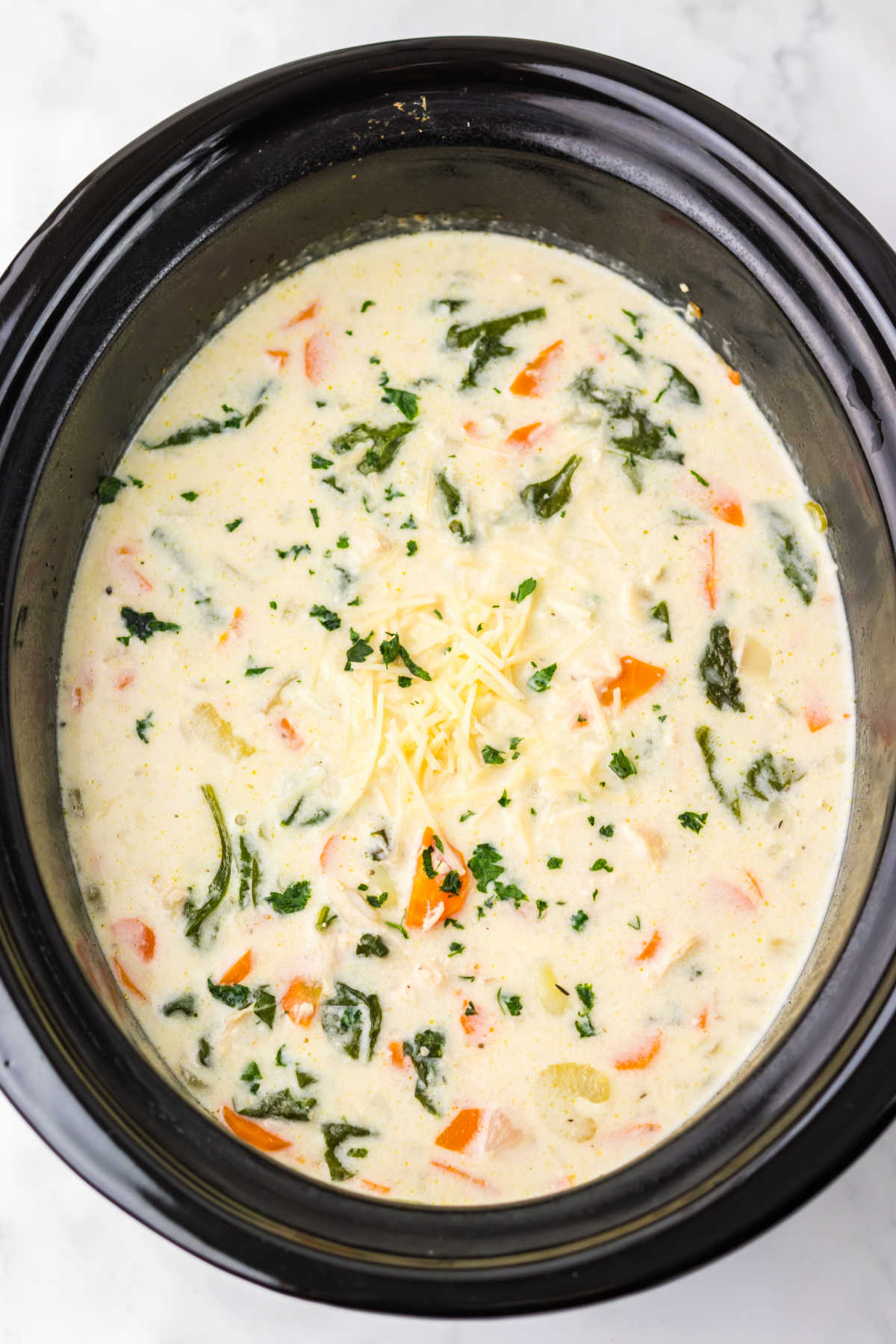 Crockpot full of creamy soup with tender gnocchi, shredded chicken, spinach, carrots, and celery, ready to be served. 