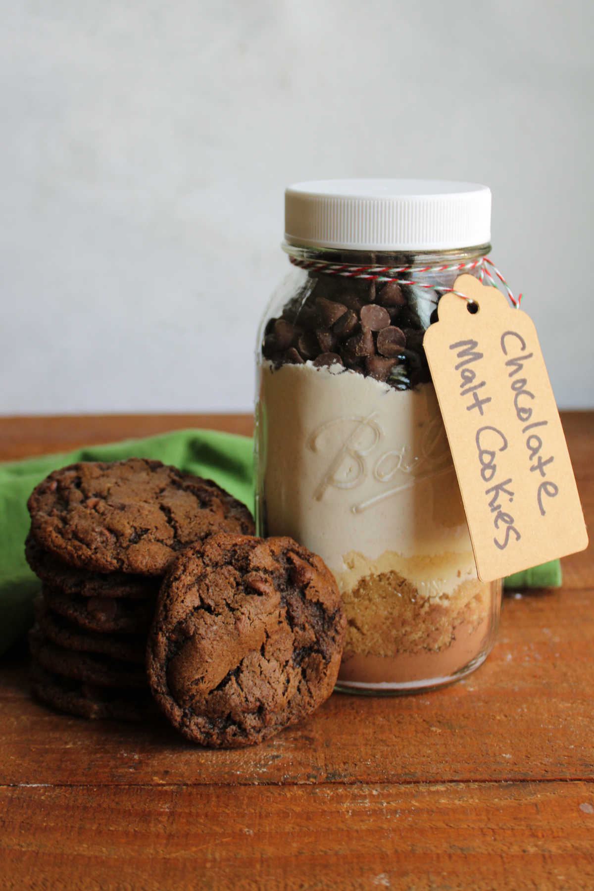 Stack of homemade malt chocolate cookies with chocolate chips next to a jar of mix used to make the cookies. 