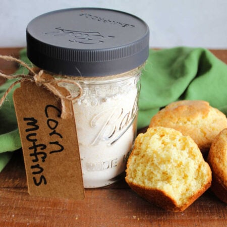 Pint jar with homemade corn muffin mix inside next to a half of a corn muffin showing the soft yellow interior.