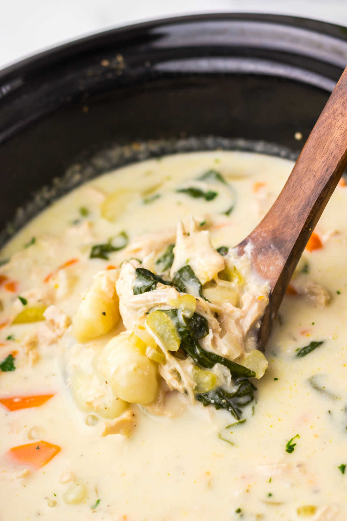 Ladle getting a scoop of creamy chicken gnocchi soup out of the crockpot it was cooked in. 