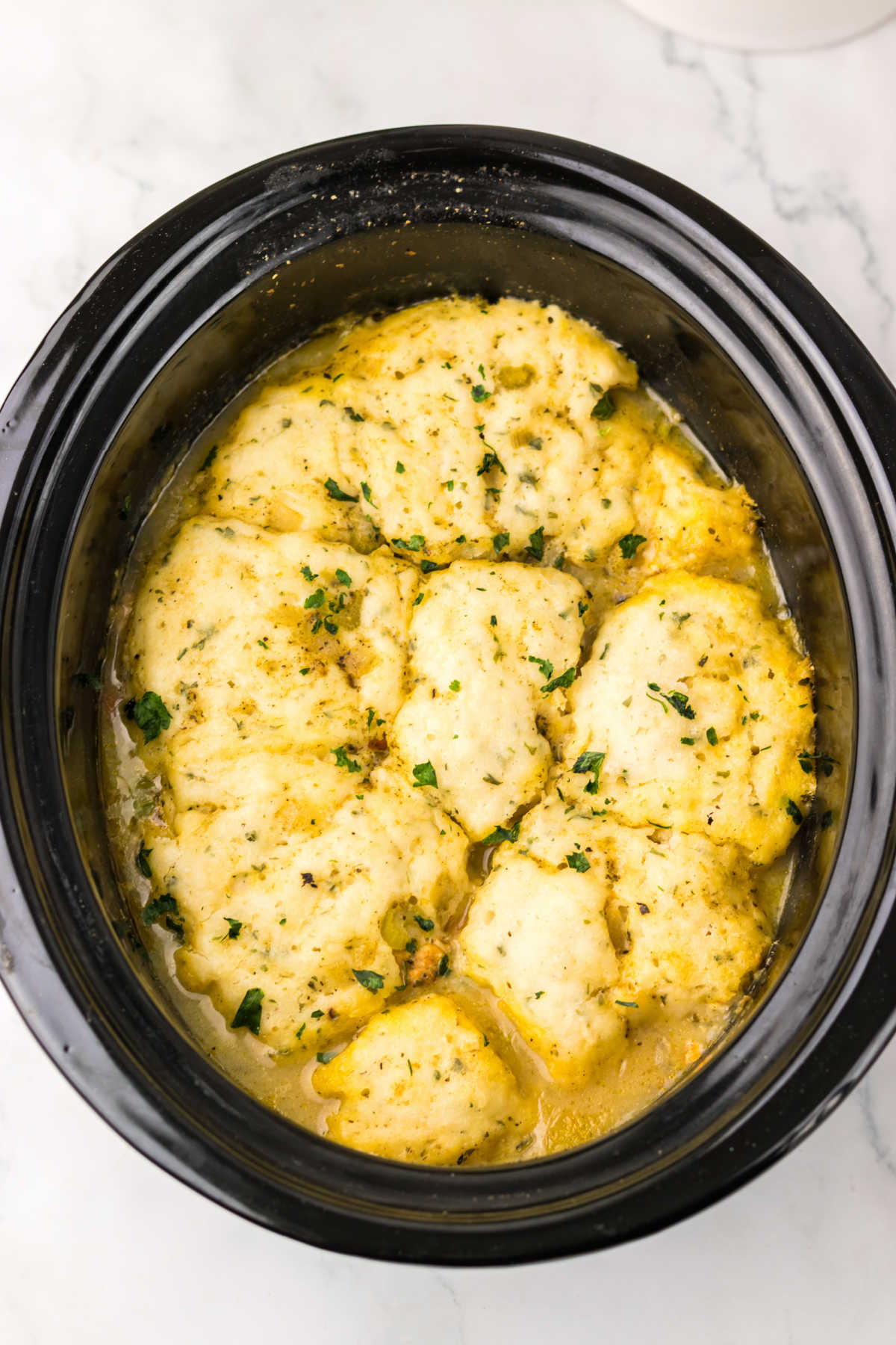 Crockpot Chicken and Dumplings 7 Crockpot filled with chicken and dumplings with creamy broth and big puffy dumplings.