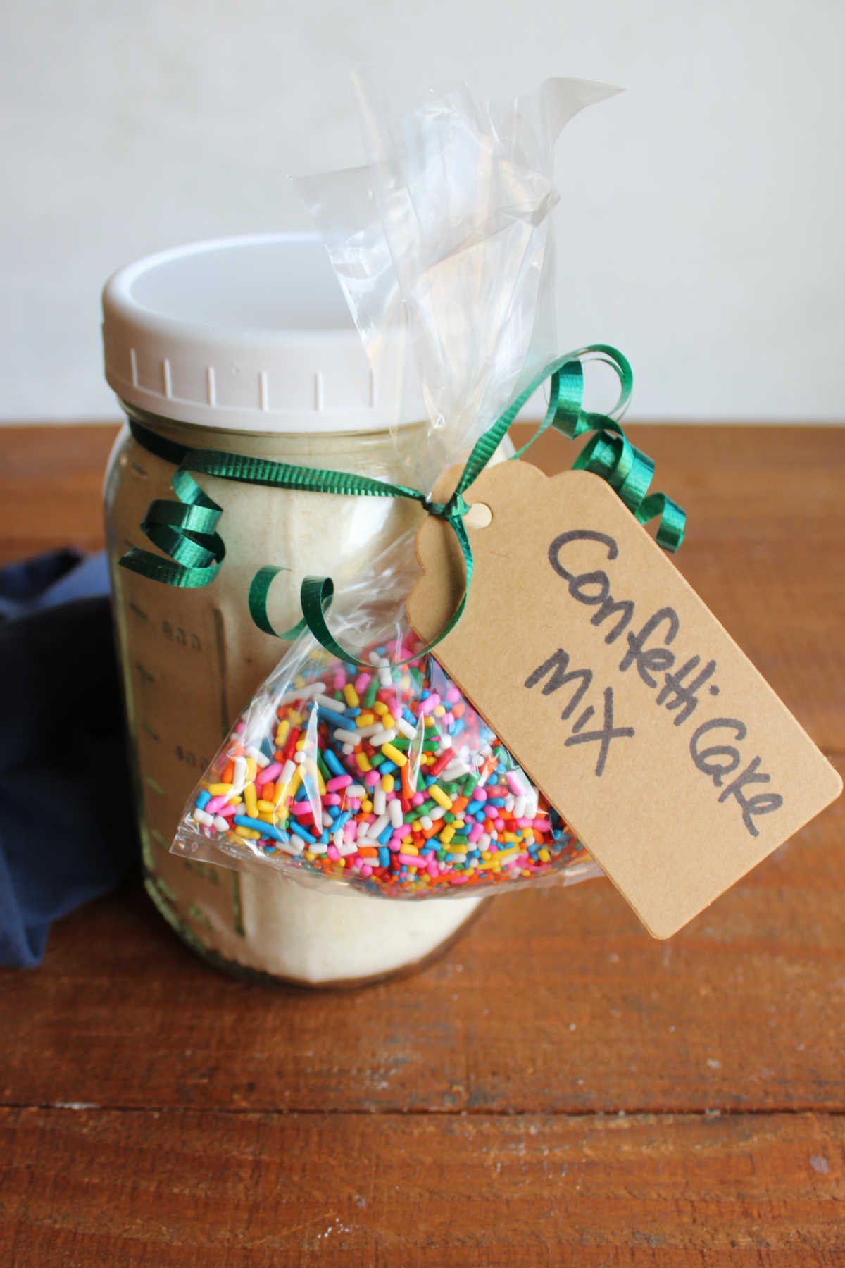 Jar of homemade cake mix with a tag that says confetti cake mix and a bag of sprinkles tied to it with curled gift ribbon.
