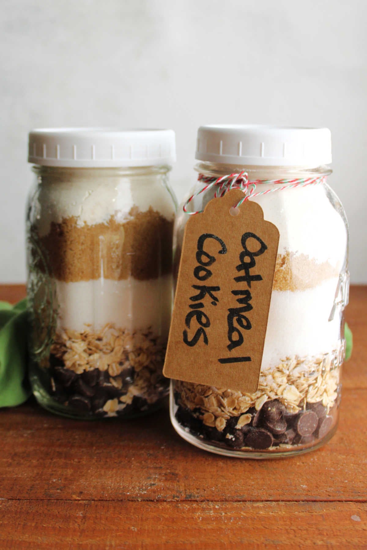 Two quart jars filled with layers of chocolate chips, oats, sugar, brown sugar, and flour to be made into oatmeal chocolate chip cookies. 